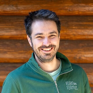 Porträt von Fabien mit einem weißen und blau gestreiften T-Shirt, gekreuzter Arm, mit einem grünen Hintergrund.